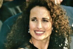 Smiling woman with curly brown hair and pearl earrings in a close-up portrait