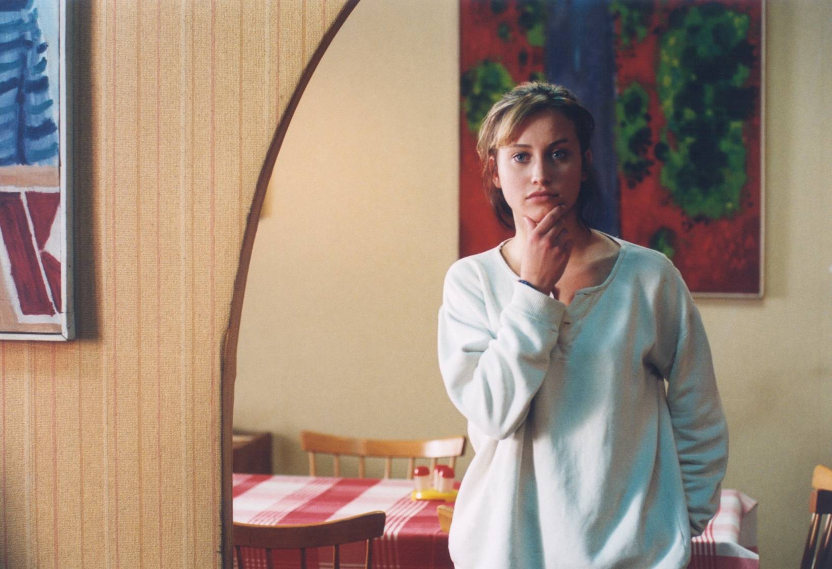 Woman stands in a cozy dining room, hand on chin, thoughtful expression.