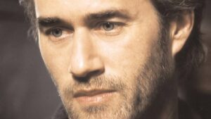 Close-up of a man's face showing blue eyes and stubble, with a serious expression.