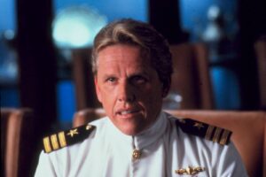 High-ranking military officer in a white dress uniform with gold insignia, speaking or reacting in a dimly lit room