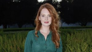 Portrait of a red-haired woman in a green button-down shirt standing in a garden.