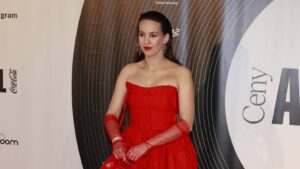 Woman in a red strapless gown with elbow-length gloves posing on a formal backdrop at a gala event.