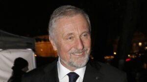 Smiling older man with gray hair and beard in a dark suit at night