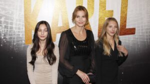 Three women posing for a photo on a backdrop with large gold letters behind them.