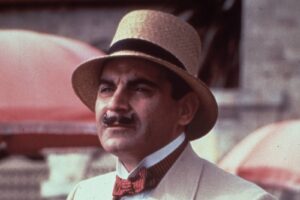 Portrait of a man with a mustache wearing a beige suit, red bow tie, and a straw hat.