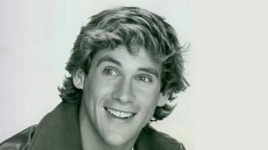 Close-up portrait of a smiling man with short, wavy hair and a leather jacket.