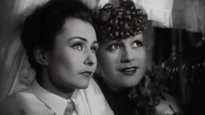 Two women in a vintage black-and-white photo, leaning close and looking upward.
