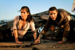Two young survivors crawl through a rubble-strewn street, dirty and distressed, looking for a way out.