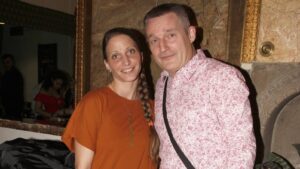 Smiling couple posing together indoors against a marble wall with a gold frame behind them.