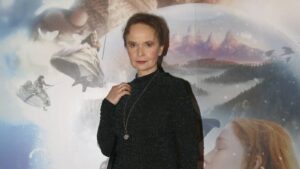 Woman posing indoors in front of a fantasy mural with mountains and figures in a snowy scene.