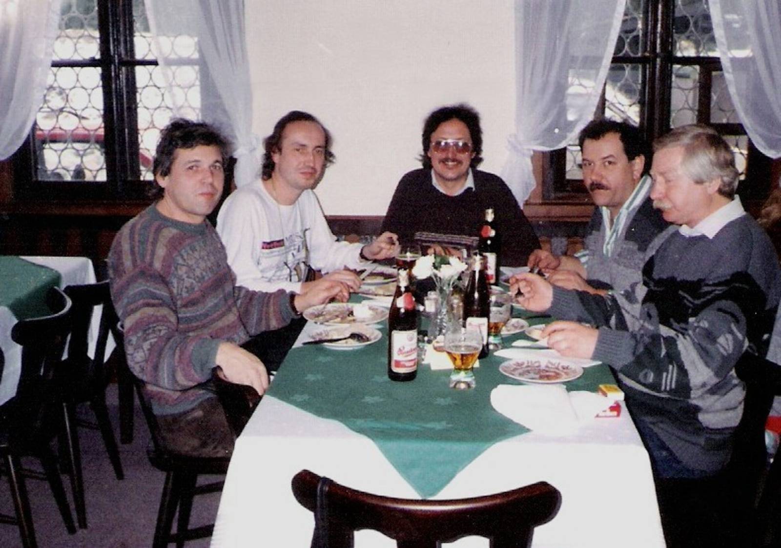 Five men sit around a restaurant table with beer bottles and plates, casually dining together.