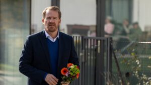 Man in a navy blazer holding a colorful bouquet outside a modern building.