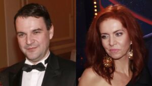 Man in a black tuxedo and bow tie posing next to a woman with red hair wearing a black dress and large gold earrings at a formal event. The left side has warm indoor lighting, the right shows a dark backdrop with lights.